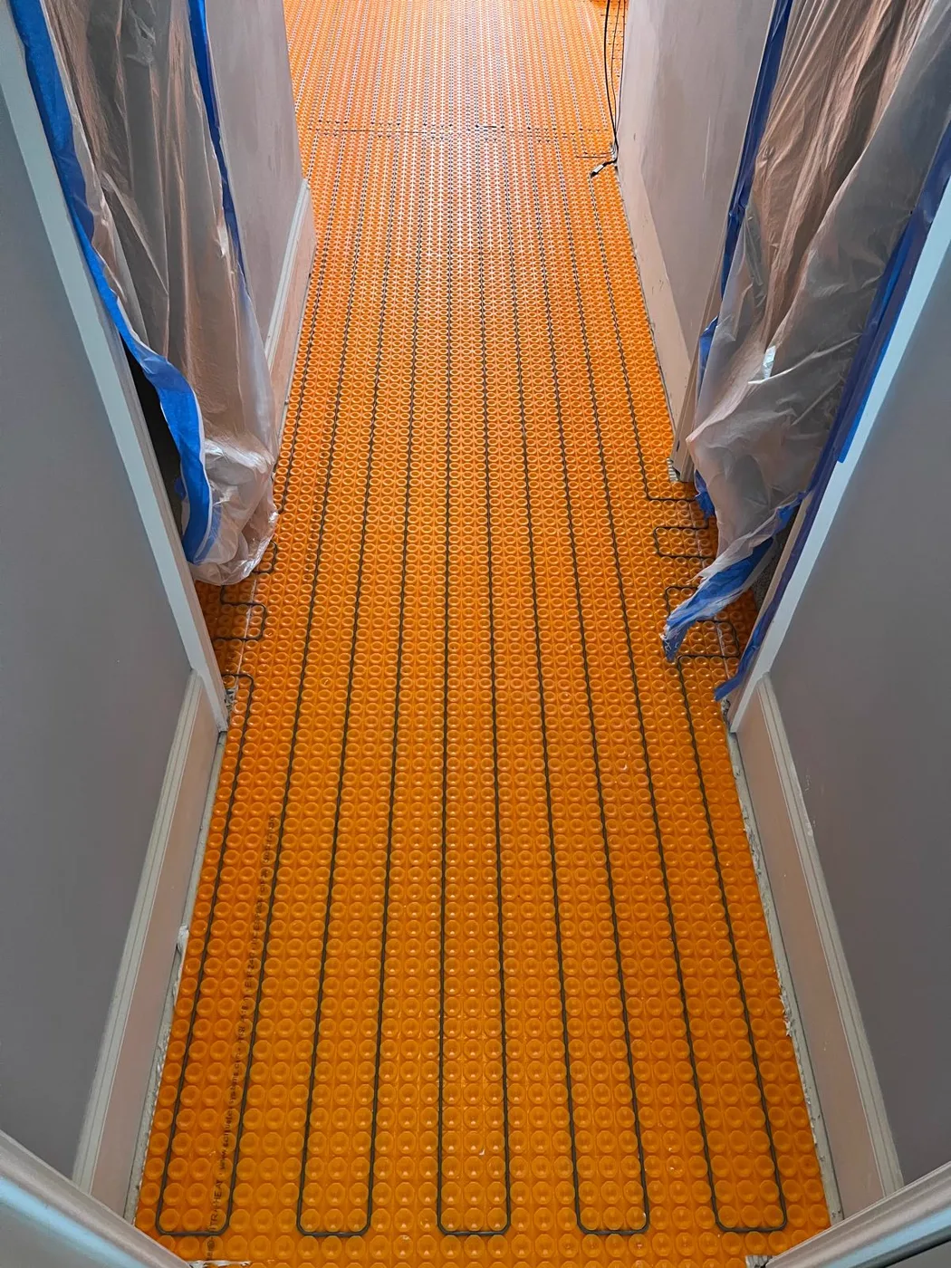 Sistema de piso radiante instalado antes del azulejo, con membrana y cables de calefacción color naranja sobre el subsuelo, remodelación de baño principal, Metro Atlanta