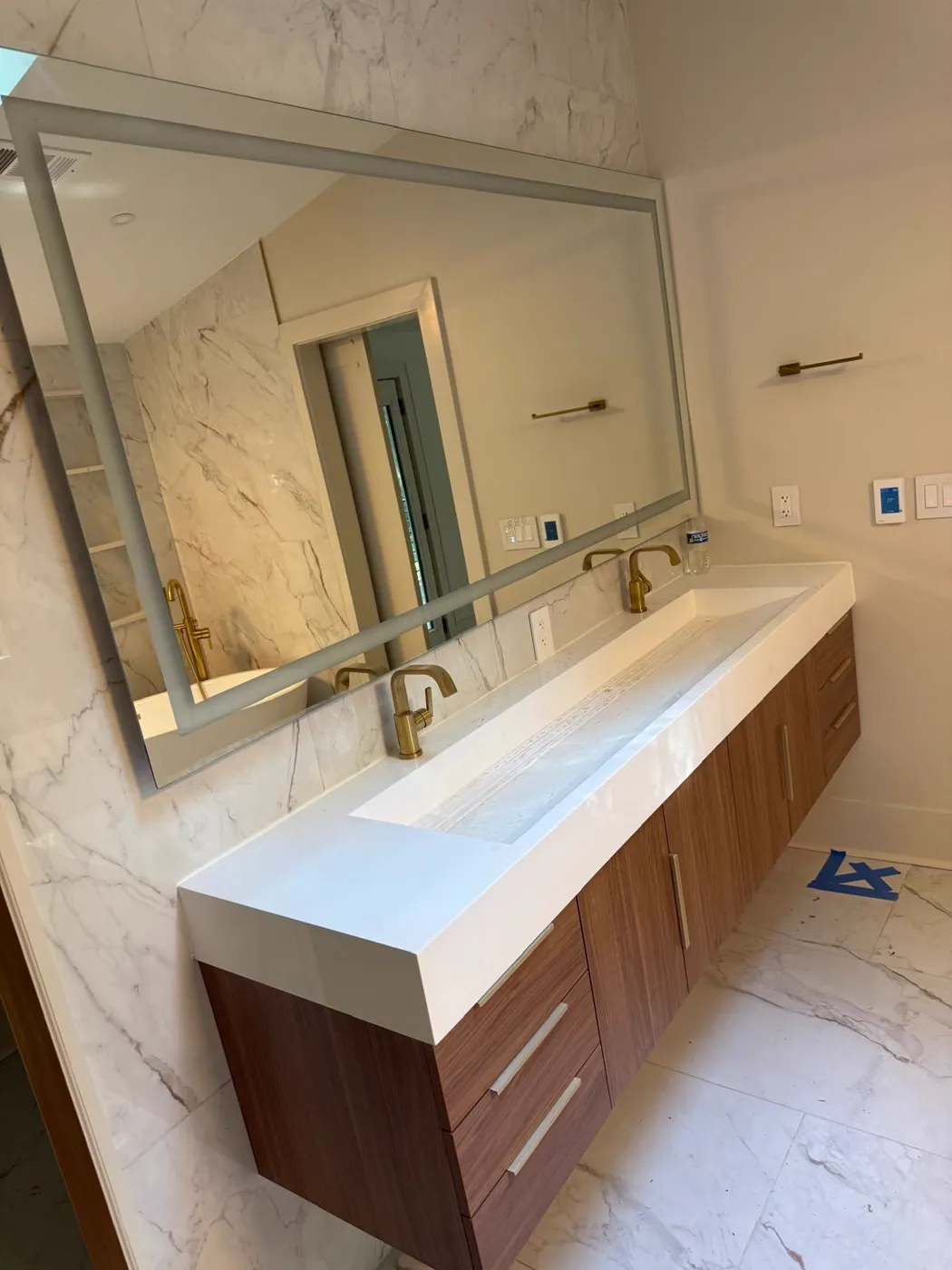 Vanidad doble flotante terminada con lavabo tipo canal, grifería dorada y espejo enmarcado sobre azulejo tipo mármol, Metro Atlanta